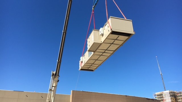 a crane lowering an electrical unit onto a building's roof